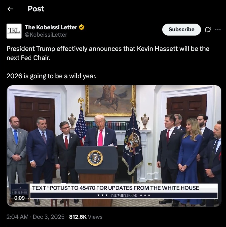 President Trump stands at a podium announcing Kevin Hassett as the likely next Fed Chair, surrounded by officials during a White House press event.